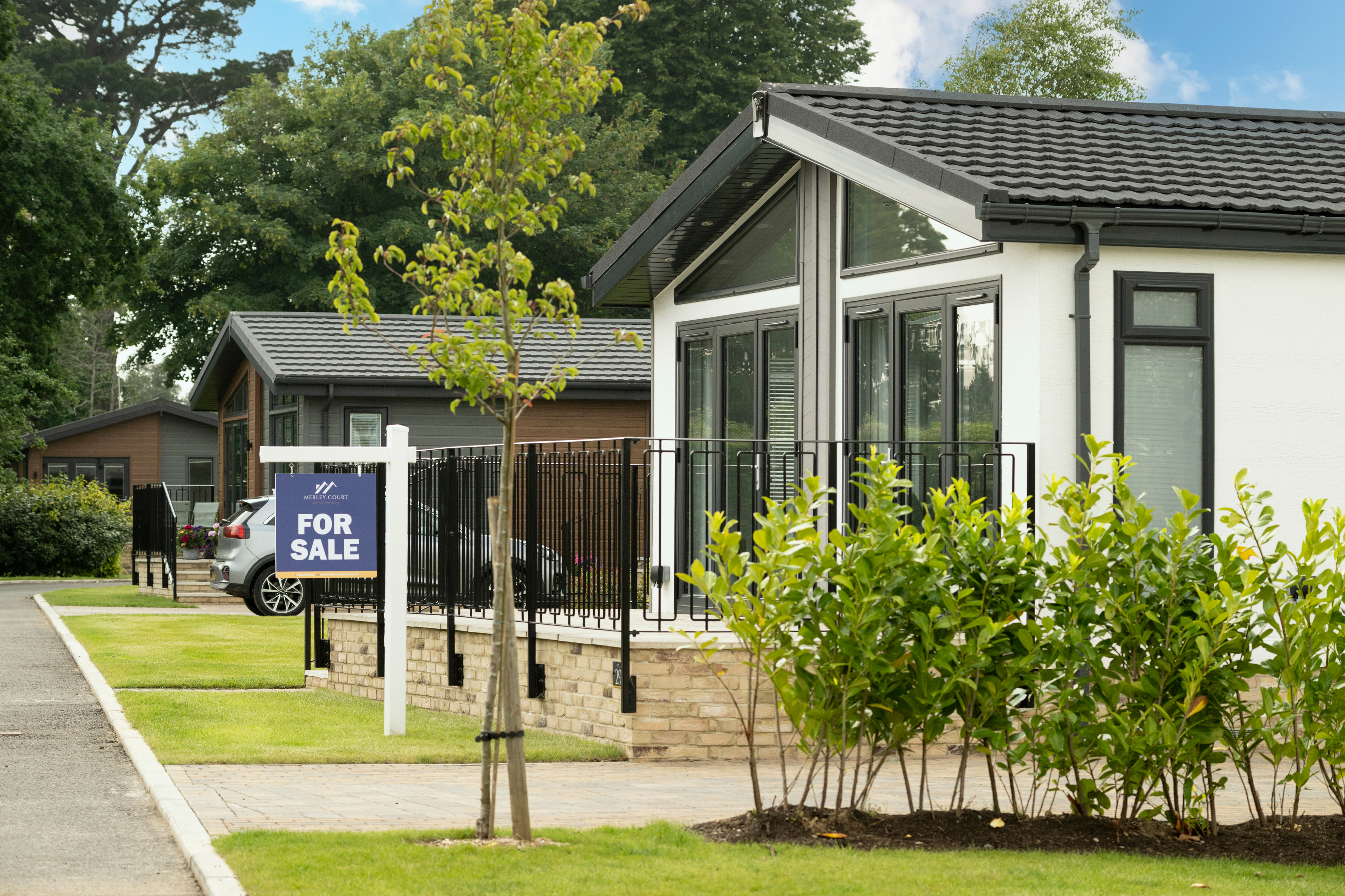 Exterior of a residential park home with raised patio and railings, surrounded by greenery and privacy hedging